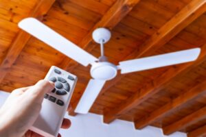 white-ceiling-fan-against-wood-roof-with-hand-changing-temperature-using-a-remote-control