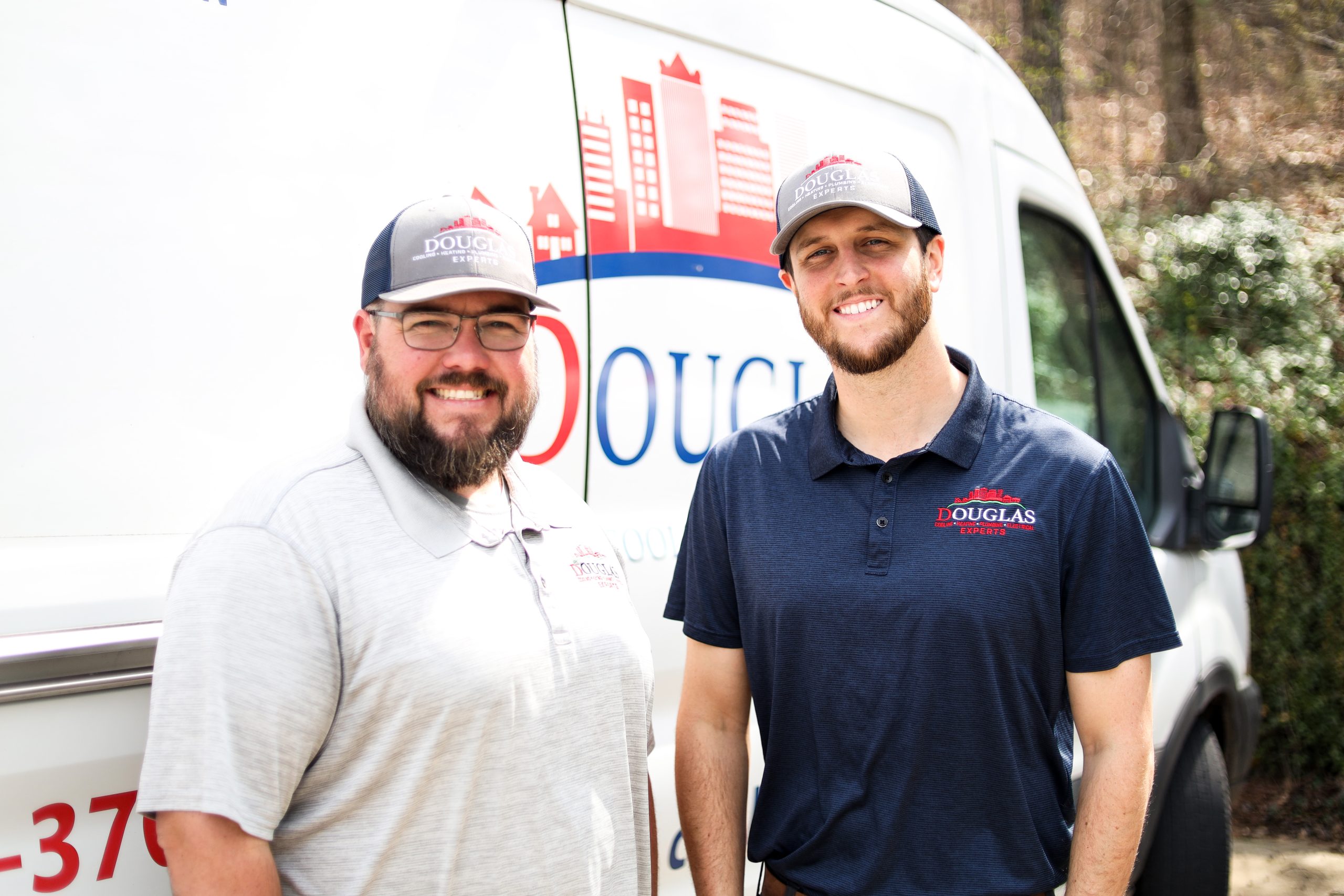 Two smiling Douglas Cooling, Heating, Plumbing & Electrical technicians standing in front of a company service van